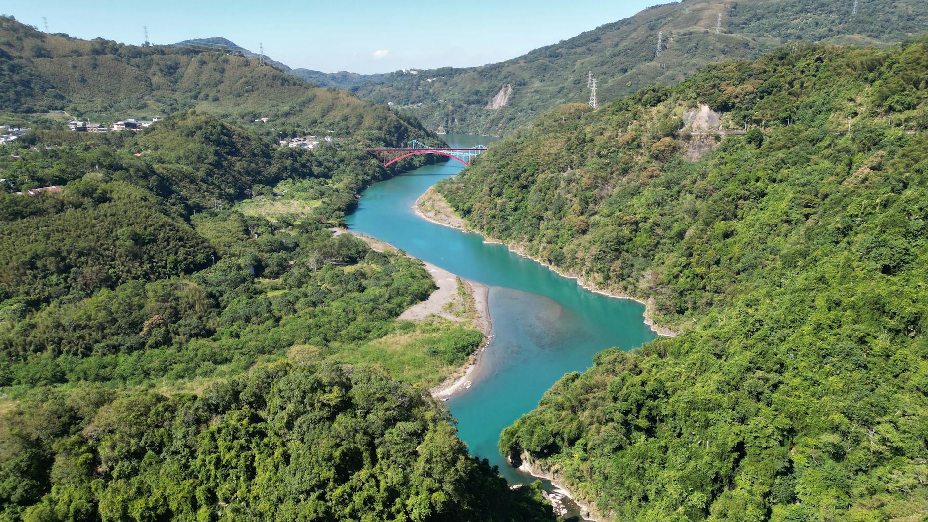 A breathtaking aerial view of a vibrant blue river winding through lush green hills under a clear summer sky.