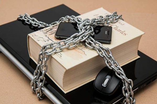 Chain-locked book, phone, and laptop symbolizing digital and intellectual security