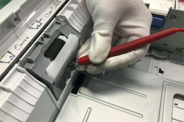 A gloved hand fixes a printer using a red precision tool, showcasing maintenance skills.