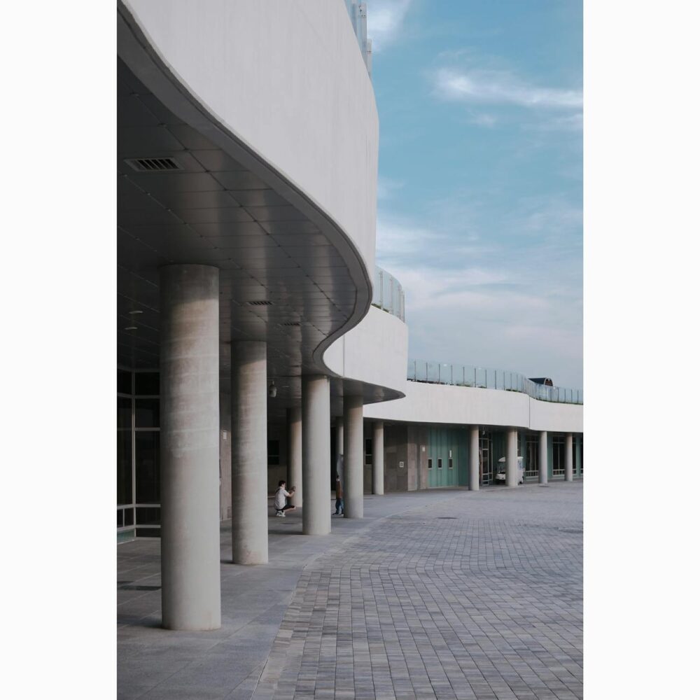 Curved concrete building facade and columns under a bright blue sky in Ansan, South Korea.