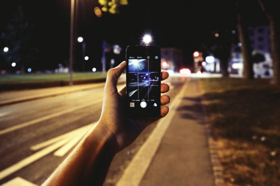 Hand holding a smartphone capturing a vibrant street scene at night.