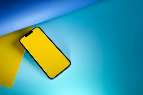 Stylish smartphone with a yellow screen on blue and yellow paper, ideal for tech and design concepts.