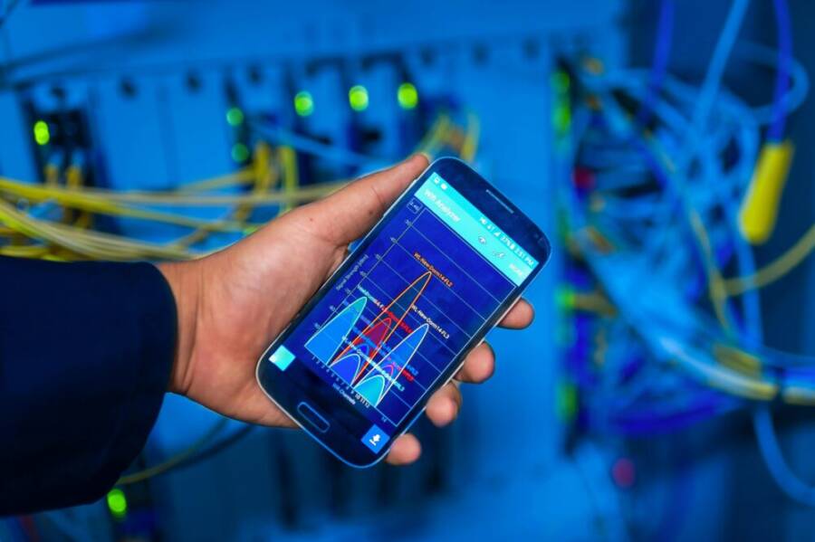 Hand holding smartphone displaying network analysis in high-tech server environment