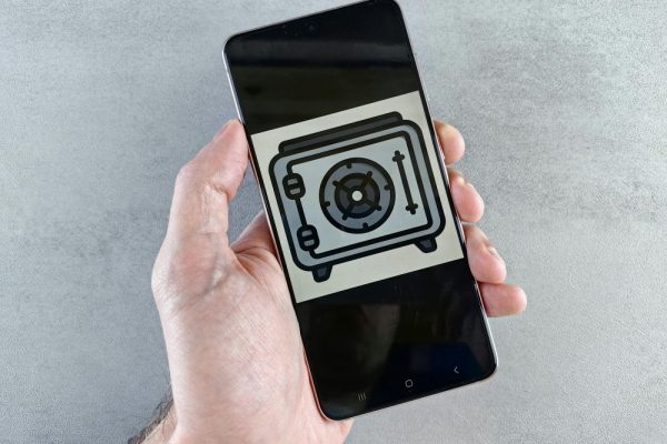Close-up of a smartphone showing a safe icon held in a hand, symbolizing digital security.