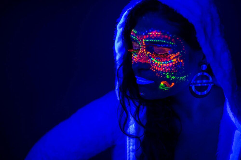 Portrait of a woman with glowing neon paint under UV light creating a futuristic effect.