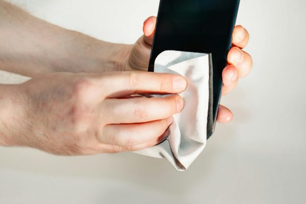 Hands cleaning smartphone screen with a soft cloth, emphasizing hygiene and device care.
