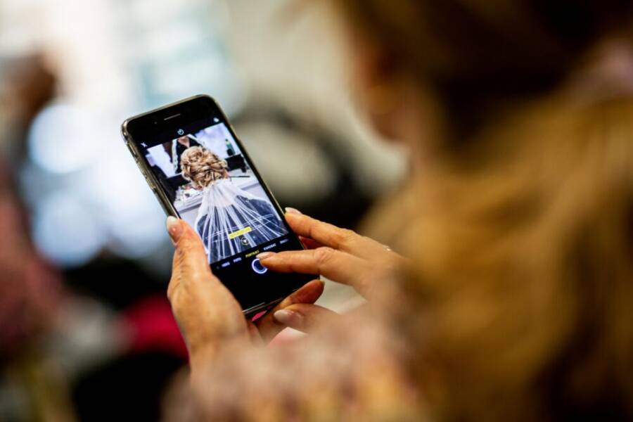 Close-up of a woman photographing a bridal hairstyle on her smartphone indoors.