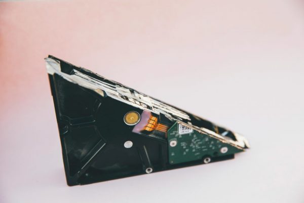 Close-up of a broken hard disk drive showing internal components on a pink background