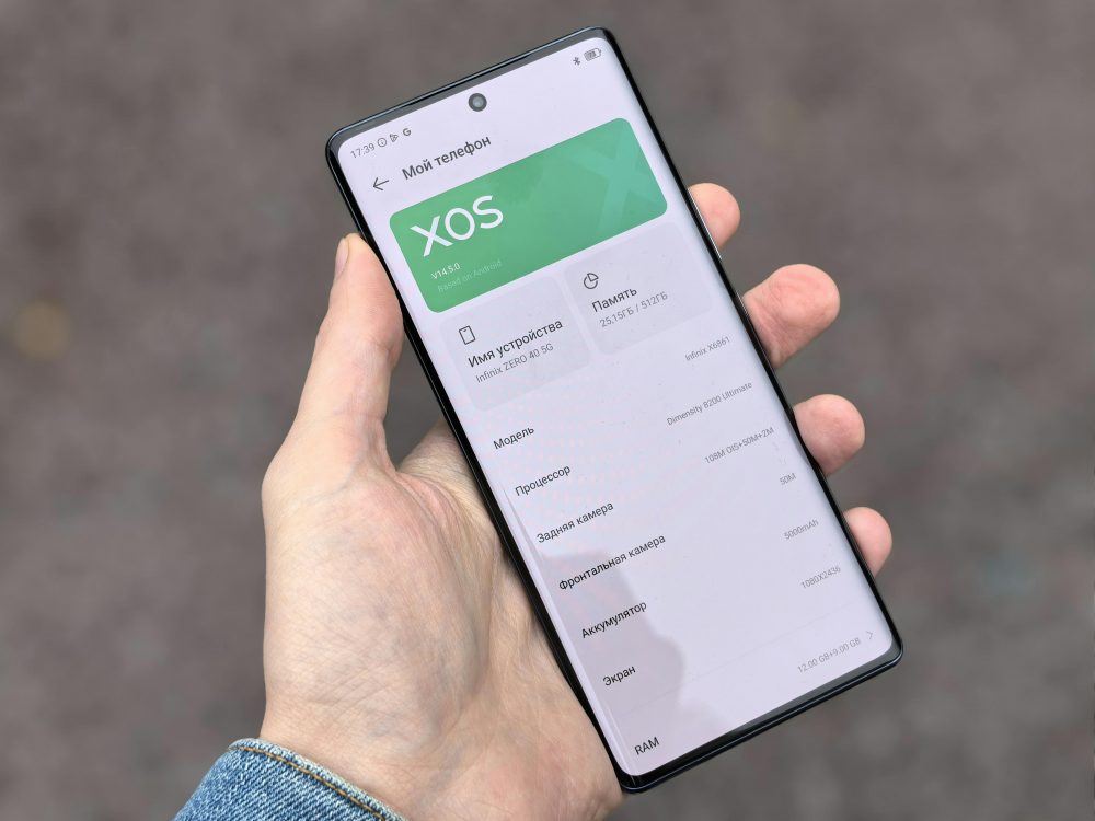 Person holding smartphone showing XOS interface on the screen, captured outdoors.