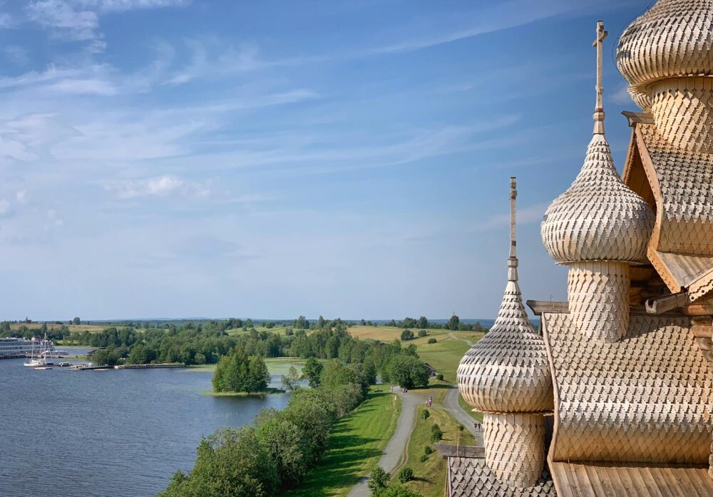 Wooden domes rise against a blue sky, overlooking a peaceful lake and lush greenery.