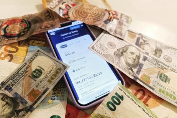 A smartphone displaying a currency converter surrounded by dollar and euro banknotes, highlighting exchange rates.