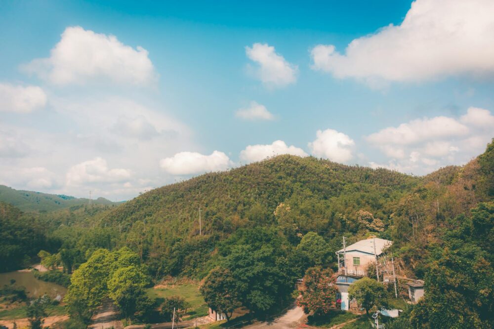 Scenic view of a rural Chinese landscape with a house, hills, and lush greenery under a bright blue sky.