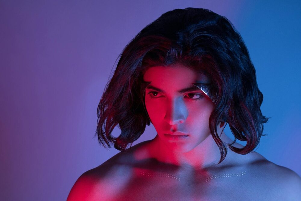 Artistic portrait of a young adult under vibrant neon red and blue lighting.