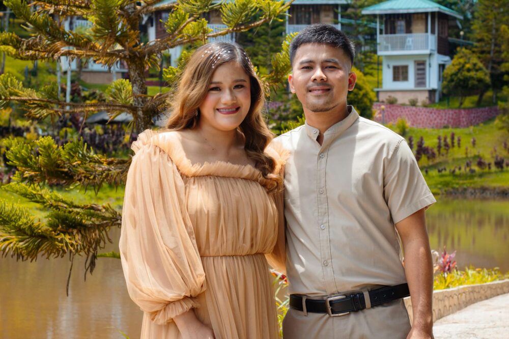 A happy couple posing outdoors with a beautiful backdrop of nature and houses.