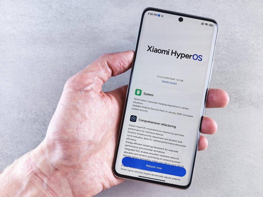 Close-up of a hand holding a Xiaomi smartphone with HyperOS interface, showcasing comprehensive refactoring and system update details.