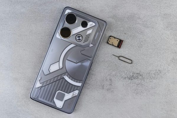 Close-up of a smartphone with futuristic design alongside a SIM card and ejector tool on a gray surface.