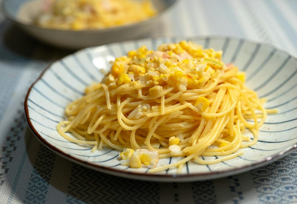 A tasty plate of spaghetti topped with sweet corn and ham, showcasing a modern gourmet dish.