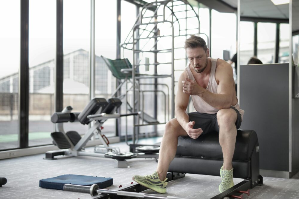 Muscular man sitting on bench in gym, reflecting after workout. Fitness and health concept.