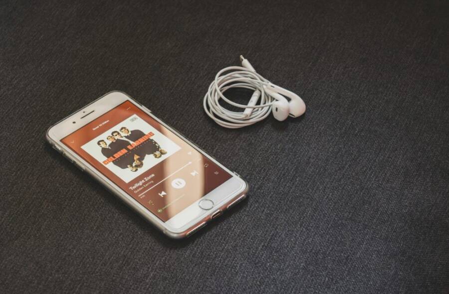 A smartphone with earbuds playing music on a sleek dark surface