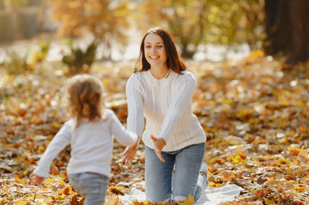 A joyful moment of a mother and daughter playing together in a park surrounded by autumn leaves.
