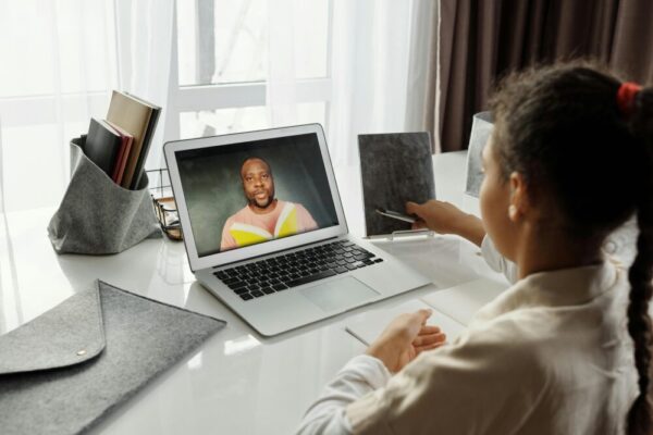 A young girl participates in an interactive online class with a teacher on a laptop, fostering education from home.