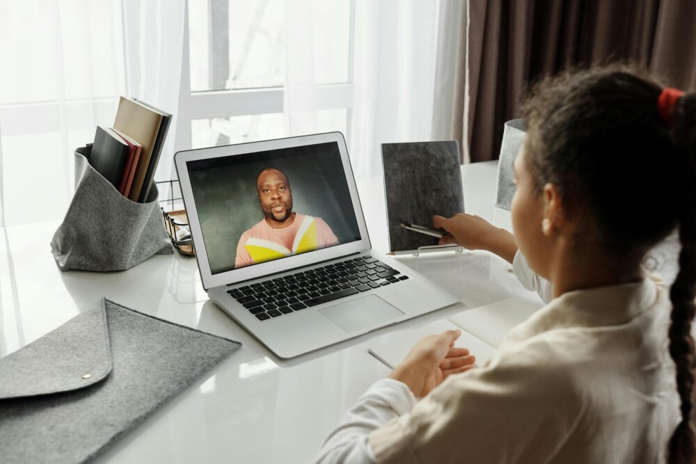 A young girl participates in an interactive online class with a teacher on a laptop, fostering education from home.