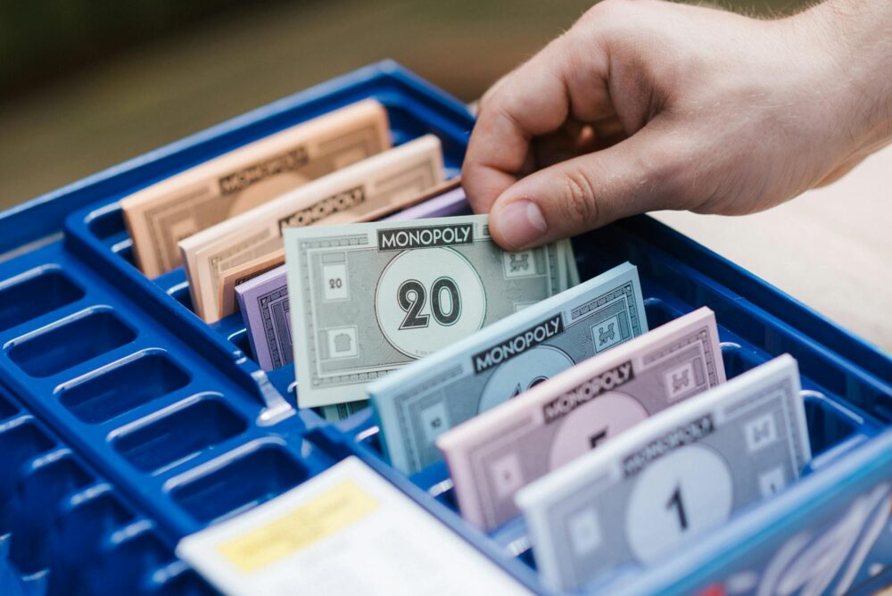 A hand organizing Monopoly game money in a blue plastic tray during gameplay.