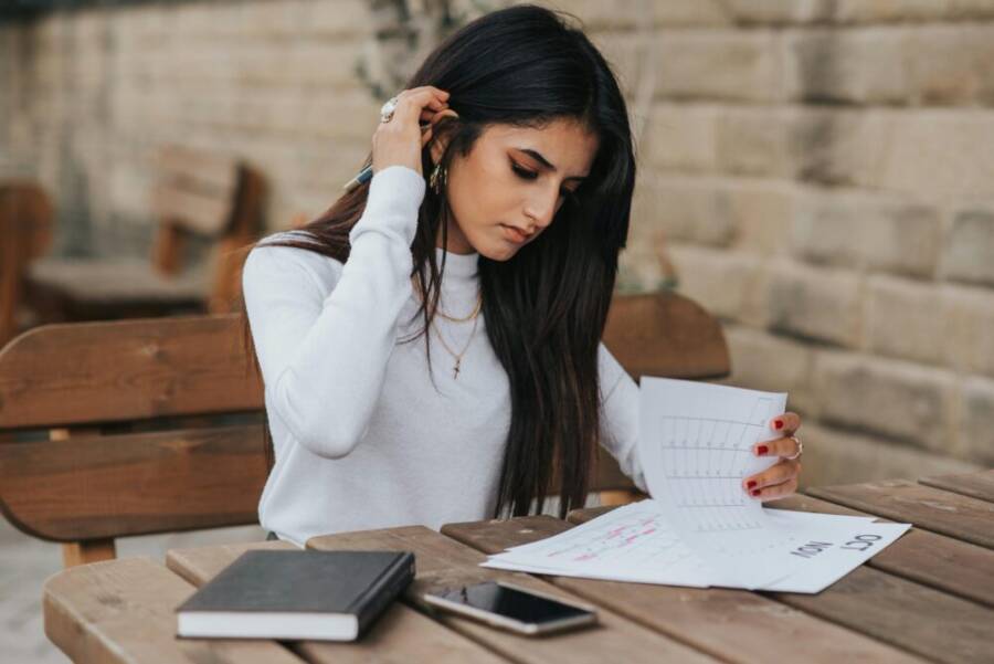 focused young woman reviewing schedule outdoors with notebook and smartphone