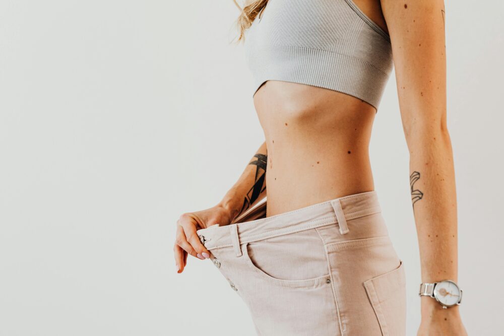 Close-up of a woman in oversized jeans symbolizing weight loss in a studio setting.