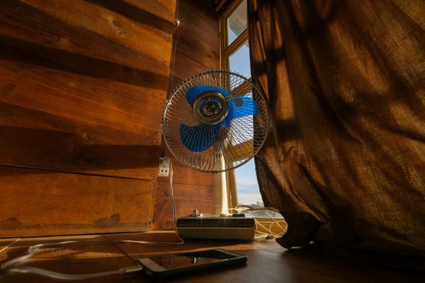 A nostalgic scene featuring an electric fan and cellphone by a sunlit curtain.