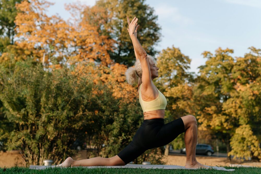 Senior woman performing yoga in a park setting during autumn season.