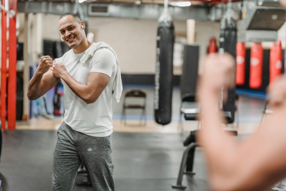 Confident man in activewear posing with a smile in a modern gym setting, exuding fitness and positivity.