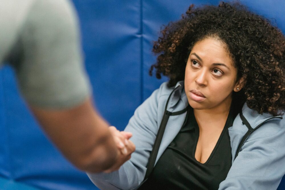 A determined woman receives motivational support in a gym setting, fostering teamwork and resilience.
