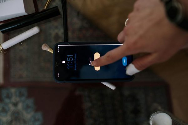 Close-up of a person touching a smartphone alarm screen with makeup items nearby.