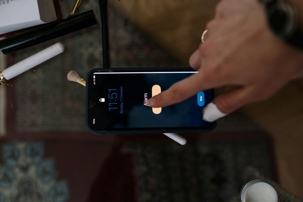 Close-up of a person touching a smartphone alarm screen with makeup items nearby.