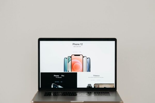 Laptop on stool showing sleek iPhone 12 ad, white background.