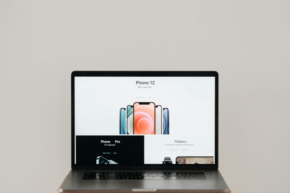 Laptop on stool showing sleek iPhone 12 ad, white background.