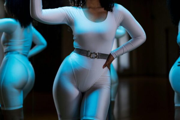 Woman in white leotard posing confidently in front of gym mirror, showcasing fitness and style.