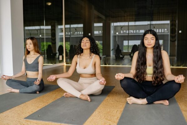 Three women practicing meditation in a yoga class indoors, promoting a calm and healthy lifestyle.