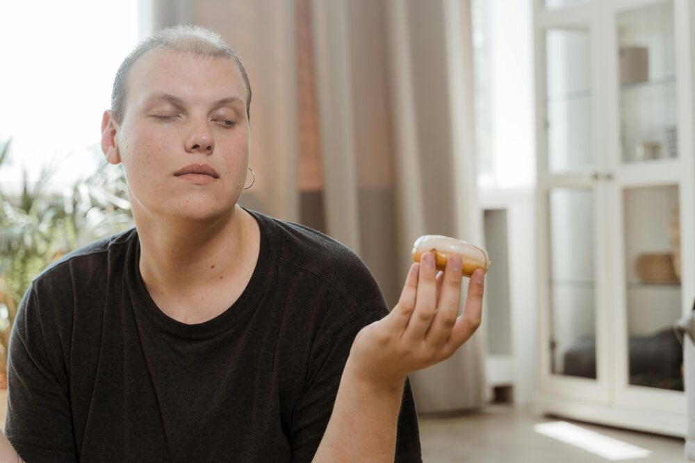 Young adult contemplating a donut while sitting indoors, showcasing a thoughtful expression.