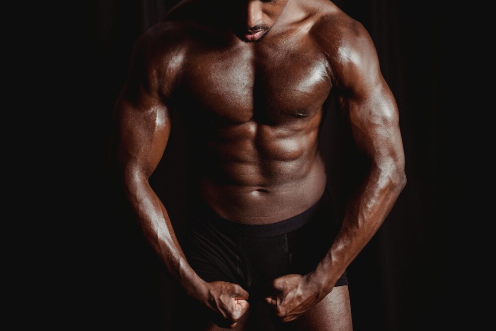 Athletic male bodybuilder flexing muscles in a dramatic studio setting, showcasing strength and physique.