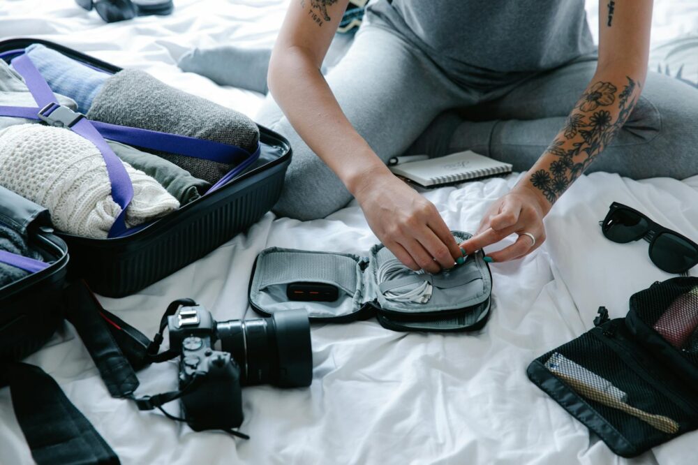 Tattooed woman packs suitcase and tech gadgets, preparing for a trip.