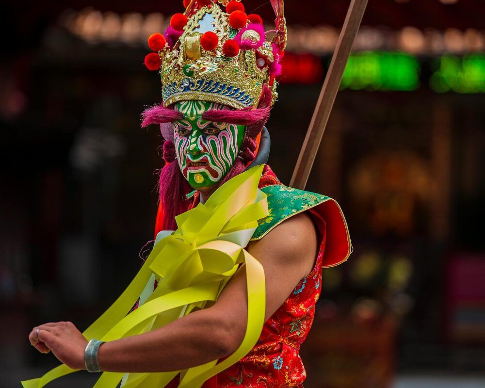 A vibrant cultural performer with intricate face paint and costume captured during a festival in Taiwan.