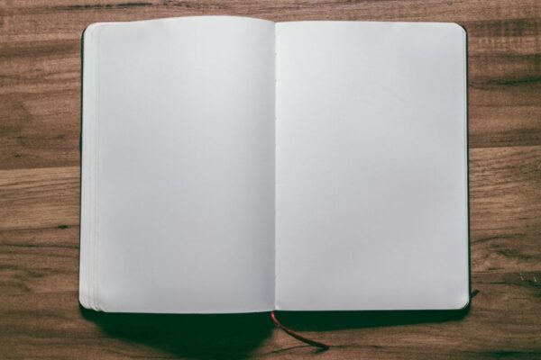 A top-down view of an open blank notebook on a wooden desk, perfect for design or writing projects.