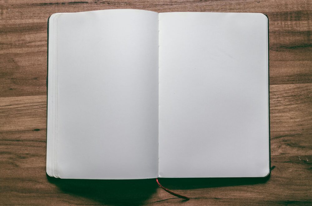 A top-down view of an open blank notebook on a wooden desk, perfect for design or writing projects.