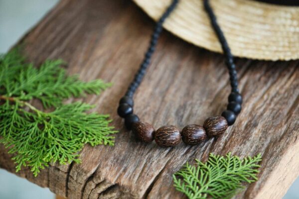 Handmade wooden bead necklace on rustic wooden surface with green leaves, evoking a natural, earthy feel.