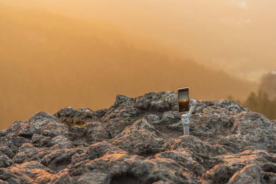 A smartphone on a gimbal capturing the serene sunrise over a rocky cliff.