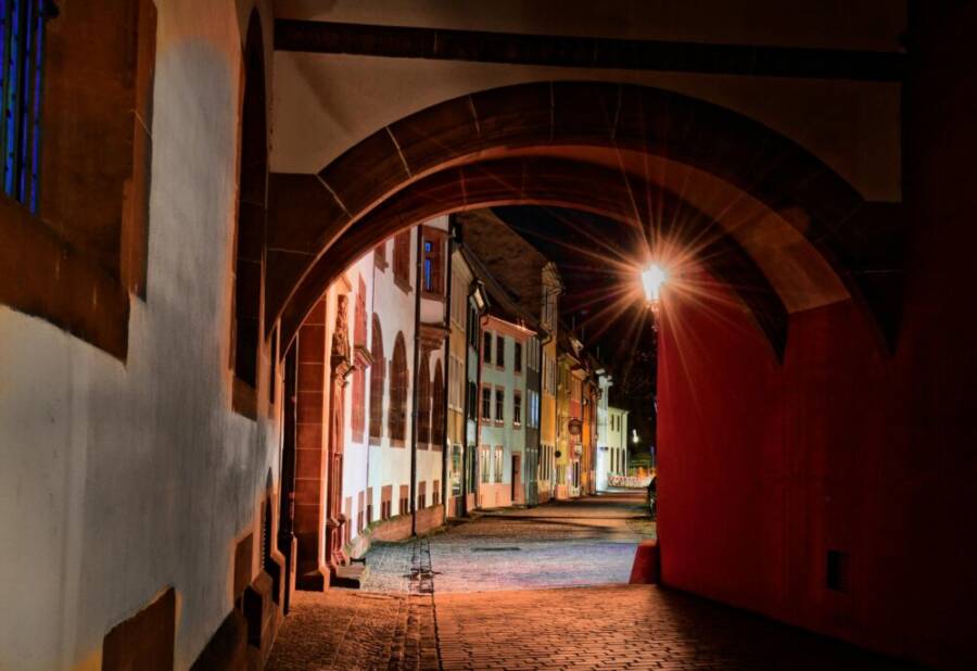 Gothic archway leading to colorful ancient street in Freiburg, Germany, illuminated at night.