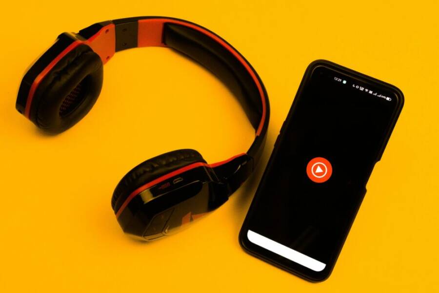 Wireless headphones and smartphone with play icon on a vibrant yellow background