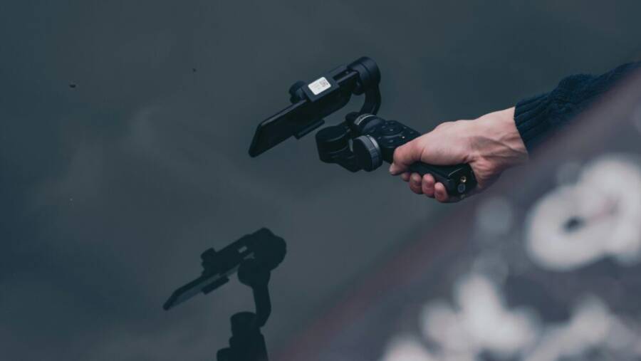 A person holding a smartphone gimbal over water, reflecting modern technology in action.